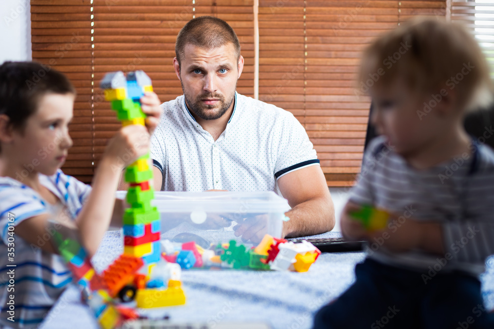 A young male dad is sadly trying to work at a computer at a remote work during the period of self-isolation in connection with the coronovirus pandemic,soft focus.Work from home with young children A young male dad is sadly trying to work at a computer at a remote work during the period of self-isolation in connection with the coronovirus pandemic,soft focus.Work from home with young children