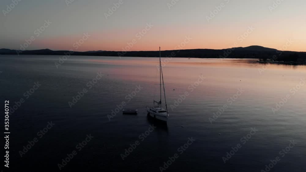 A Lonely Yacht Anchored On The Glacial Lake. Colorful Sunset Over Lake Memphremagog And Mountains. - aerial drone circling A Lonely Yacht Anchored On The Glacial Lake. Colorful Sunset Over Lake Memphremagog And Mountains. - aerial drone circling