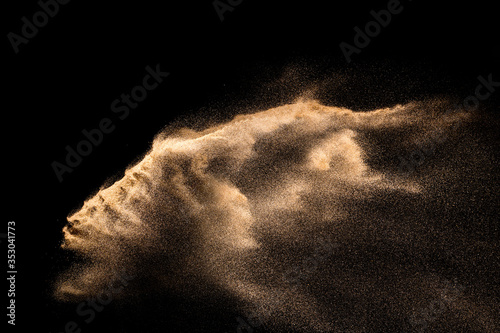 Golden sand explosion isolated on black background. Abstract sand cloud. Golden colored sand splash against dark background. Yellow sand fly wave in the air. photo