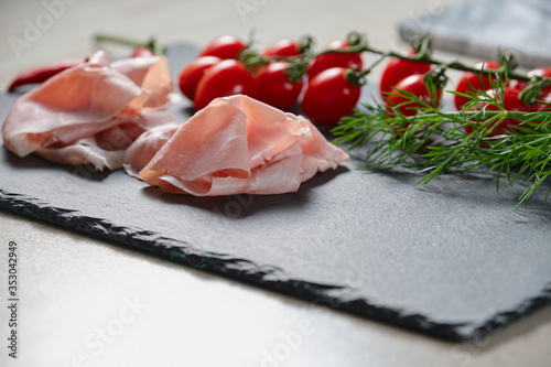 Baked ham, cherry tomatoes, red pepper on a black stone, close angle, blurred background
