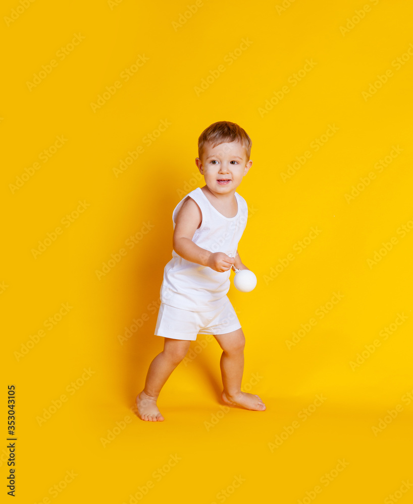 little boy in a t-shirt and underpants on an orange-yellow background with a white Christmas ball in his hands little boy in a t-shirt and underpants on an orange-yellow background with a white Christmas ball in his hands