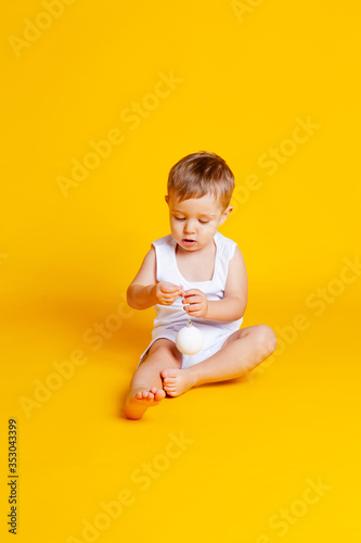 little boy in a t-shirt and underpants on an orange-yellow background with a white Christmas ball in his hand