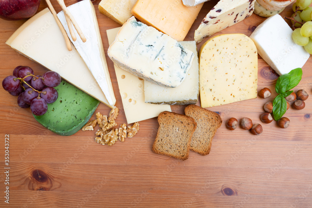 Blue, green, spicy different cheeses and snacks set. Slices of bread, grapes and nuts on brown wooden table. Top view, copy space. Cheese dairy concept