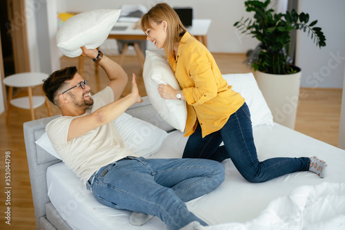 Young couple fighting pillows on the bed. Happy couple having fun at home.	 photo