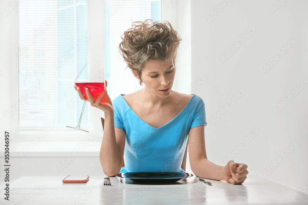 Young woman sitting at the table by the window and holds a glass of red wine in her hand Young woman sitting at the table by the window and holds a glass of red wine in her hand