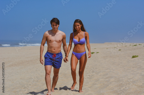 Beach couple walking on romantic travel vacation summer holidays romance. Young happy lovers, Latin woman and Caucasian man holding hands embracing outdoors.