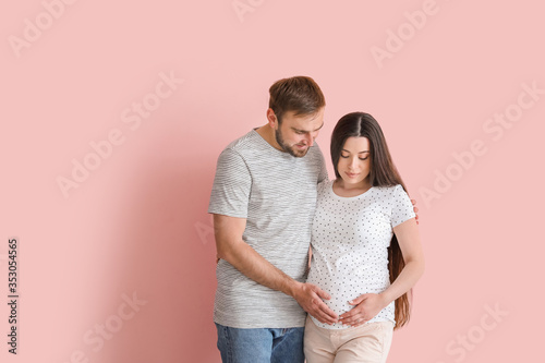 Beautiful pregnant woman with husband on color background