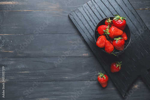 Bowl with ripe strawberry on dark background