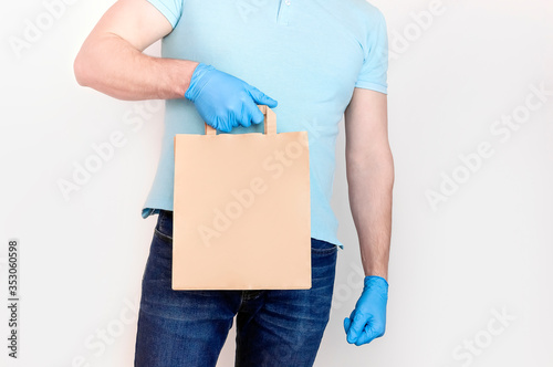 Delivery against Coronavirus 2019-nCov in pandemic Contactless delivery. Male hand in blue medical gloves holds craft paper bag on white background. Concept of delivery of goods food during quarantine