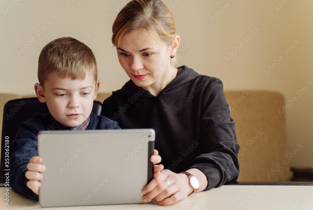 Mother using laptop and tablet teaching with her son online at home in his room Mother using laptop and tablet teaching with her son online at home in his room
