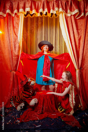 Family during a stylized theatrical circus photo shoot in a beautiful red location. Models grandmother and granddaughter posing on stage with curtain