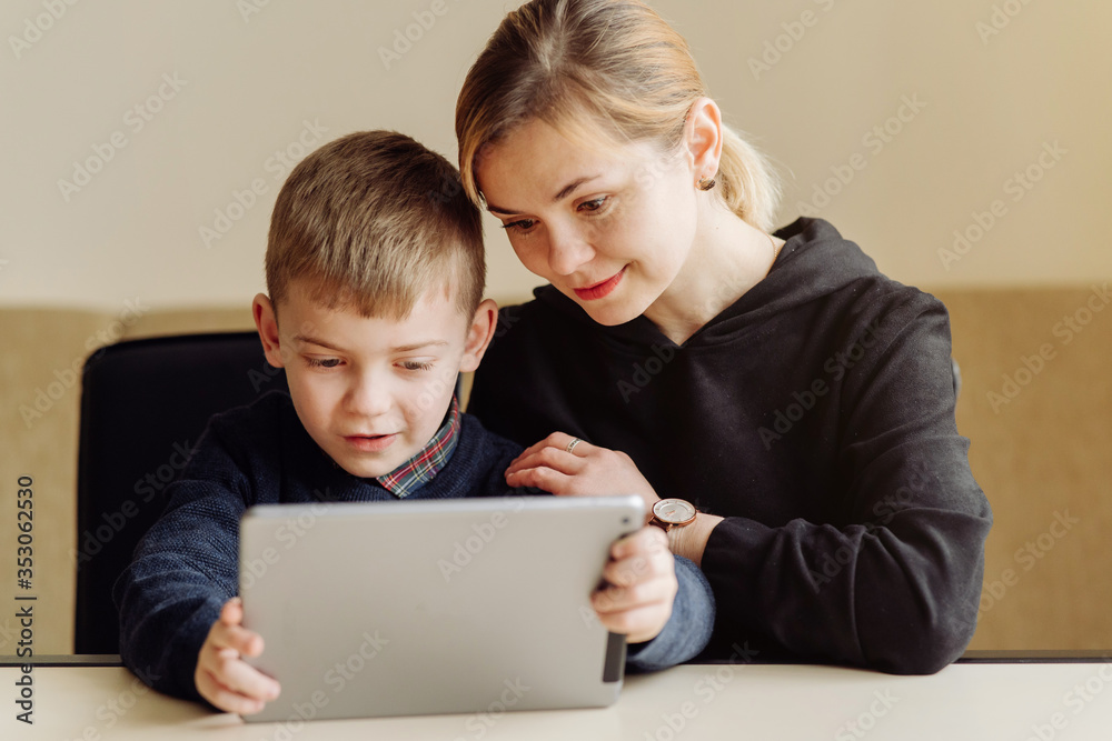 Mother using laptop and tablet teaching with her son online at home in his room Mother using laptop and tablet teaching with her son online at home in his room