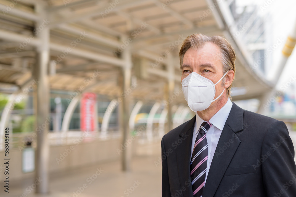 Face of mature businessman with mask thinking at the skywalk bridge
