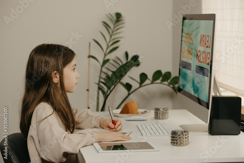 Distance learning. A young girl with long hair studying remotely online. A female child learns a lesson diligently using an all-in-one computer at home. Home education. photo