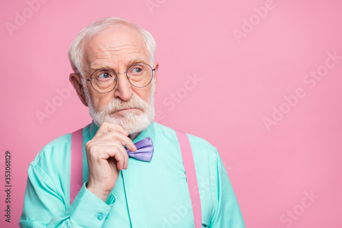 Closeup photo of attractive stylish grandpa holding hand on chin look up empty space minded wear specs mint shirt suspenders violet bow tie isolated pink pastel color background