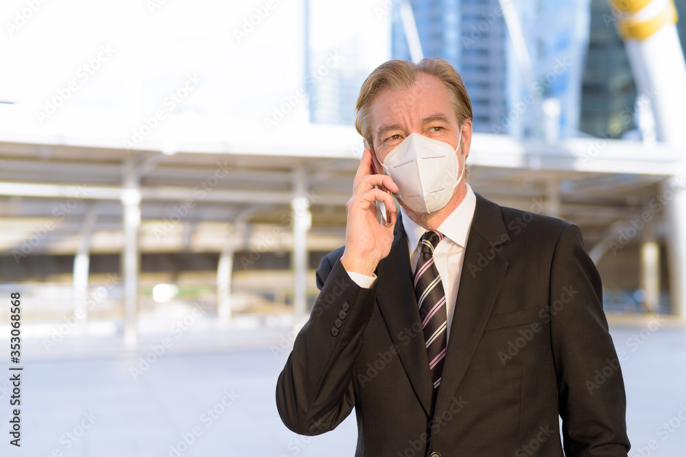 Mature businessman with mask thinking while talking on the phone at skywalk bridge Mature businessman with mask thinking while talking on the phone at skywalk bridge