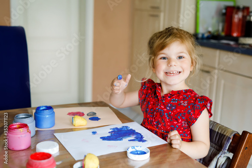 little toddler girl painting with finger colors and potato stamp during pandemic coronavirus quarantine disease. Happy creative child, homeschooling with parents