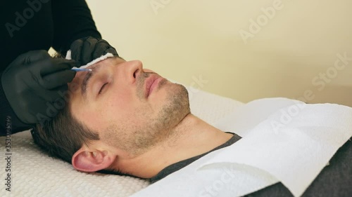 Close up of cosmetologist making permanent makeup. Microblading procedure. High quality close-up 4k slow motion video of a man laying on a couch during the esthetician brow microblading treatment.