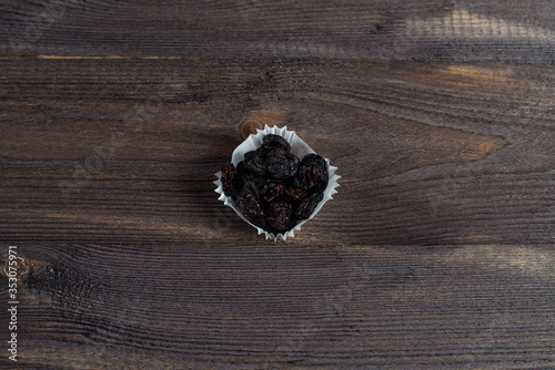 A portion of black raisins in a paper muffin cup on a dark wood background.