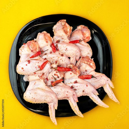 raw chicken wings with spices, pickled with hot pepper, on black plate, bright yellow background
