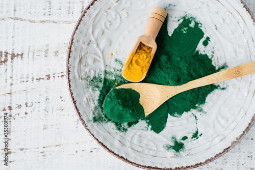 Spirulina and turmeric powder in wooden spoons