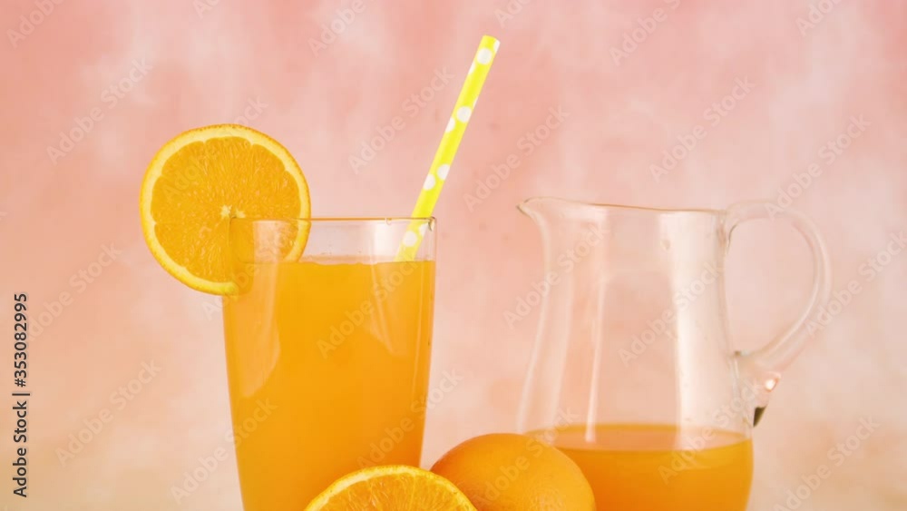 Fresh squeezed orange juice in glass and jug on pastel background with sliced orange Fresh squeezed orange juice in glass and jug on pastel background with sliced orange