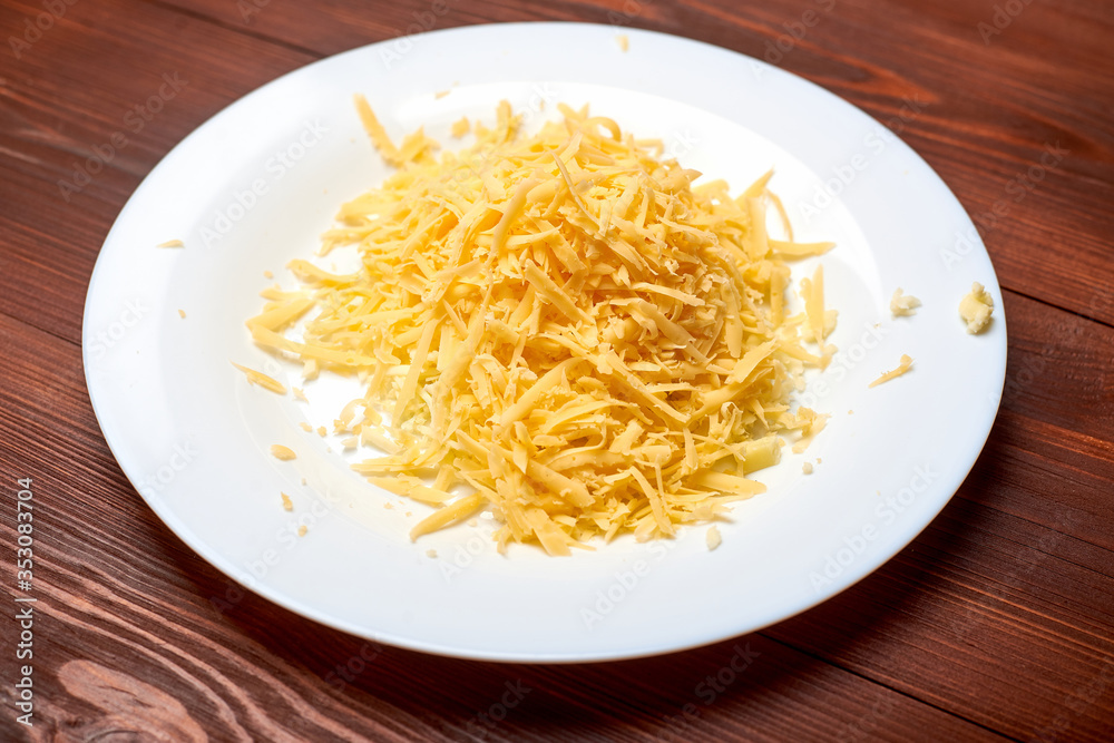 Grated cheese on a plate on a dark wooden background. Preparation for cooking.