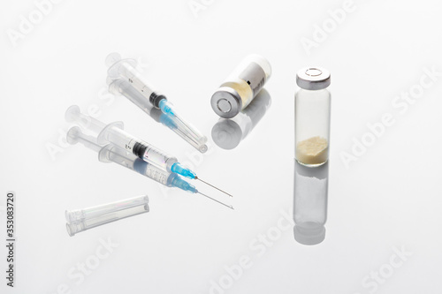 Two medical syringes with an injection needle, vials with medicine on a medical table.