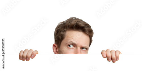 Fotografie Young man with surprised eyes peeking out from behind billboard paper poster