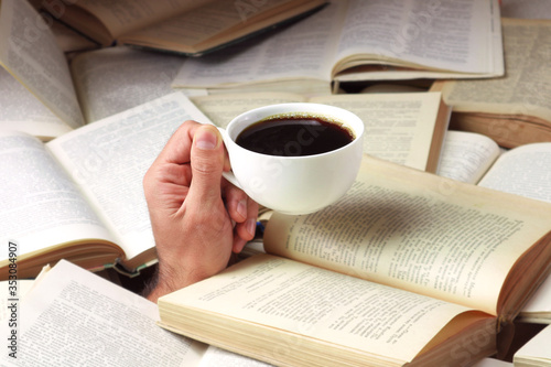 Man bombarded with open books with a cup of coffee in hand. A man buried in literature.