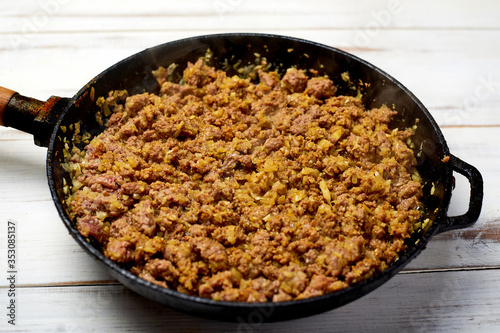 Grilled minced meat with onions, spices and cream in a pan on a light wooden background. Cooking toppings.