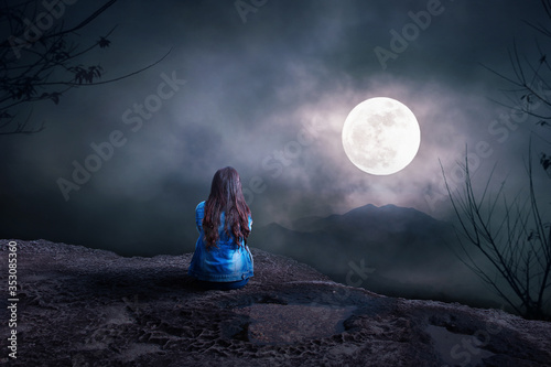 Young Woman sitting alone on the mountain to watch the full moon at night, nature background, Back view