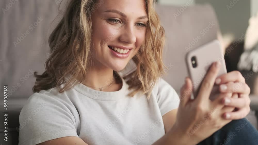 Young cheery woman indoors at home using mobile phone