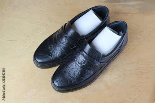 Black men's shoes on a wooden surface.