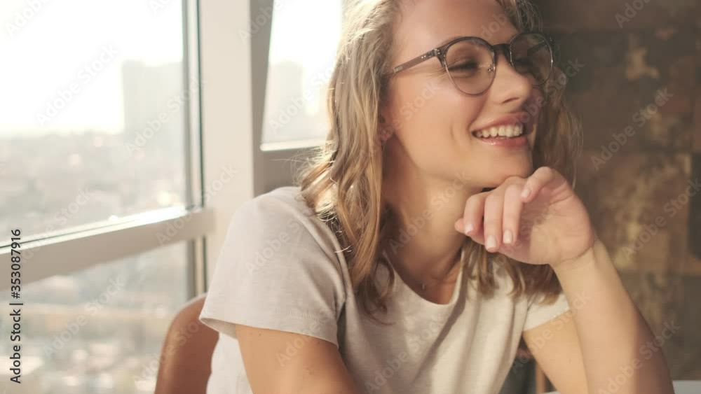 Young optimistic woman indoors at home wearing eyeglasses near window Young optimistic woman indoors at home wearing eyeglasses near window