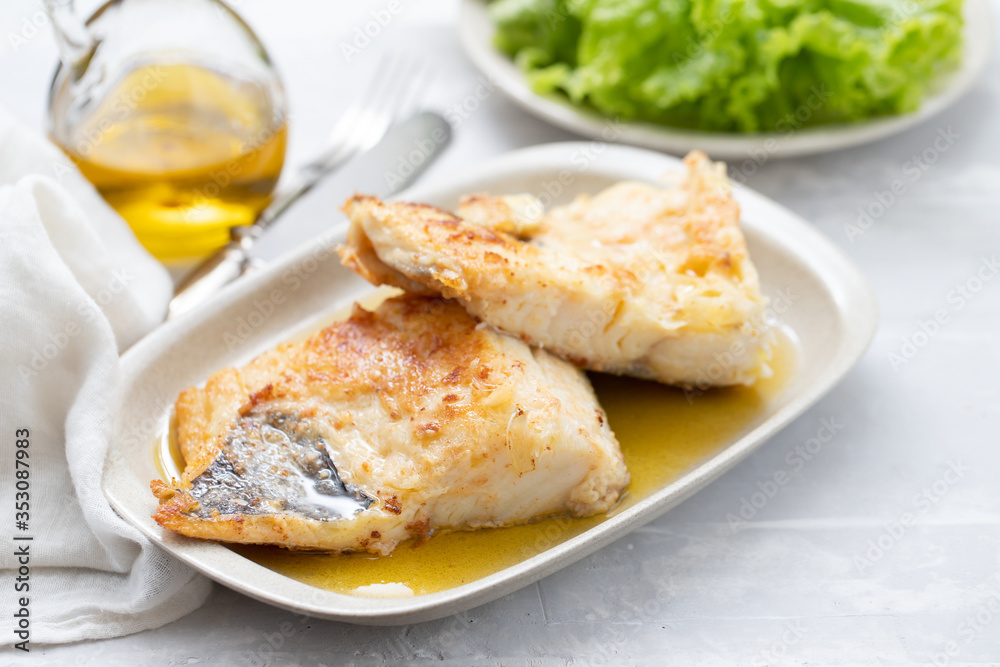 fried cofish with garlic and olive oil on white dish on ceramic background