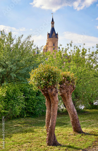 Schwerin Castle behind green trees under a blue sky.