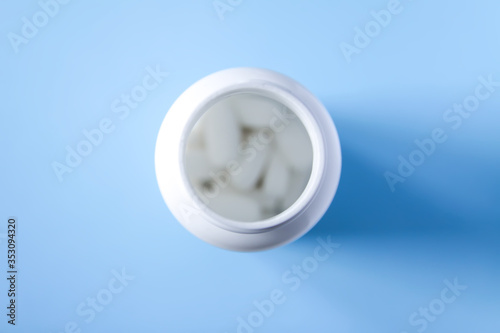 Pills of vitamin in the opened white plastic container on soft blue background. photo