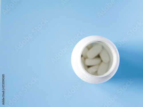 Pills of vitamin in the opened white plastic container on soft blue background.
