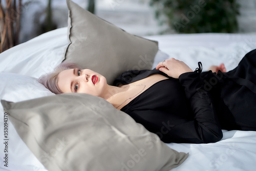 a young woman with ashy hair and a short haircut in a black evening dress. teen girl lies on a bed with several pillows