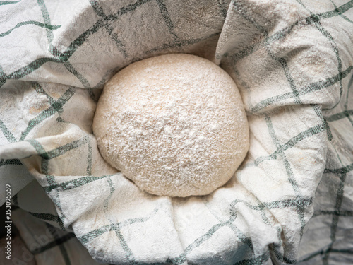 Traditional home made sourdough bread proofing in basket covered with tea towel in kitchen before bake