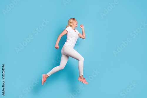 Full length profile photo of attractive funny crazy lady jump high up running speed rushing shopping center wear casual white s-shirt pants footwear isolated blue color background