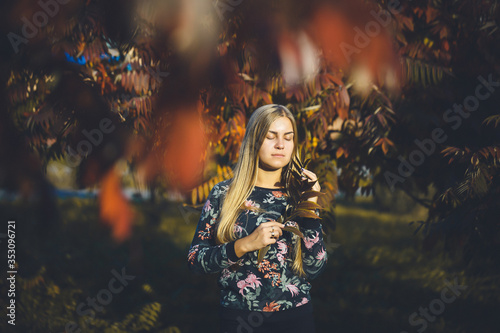 Woman girl long-haired blonde in a forest with trees with red leaves. She is happy confident in a photo shoot. Autumn park sunny warm day. Romantic concept.