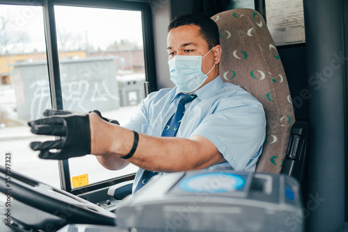 young hispanic bus driver wears gloves and mask to protect himself