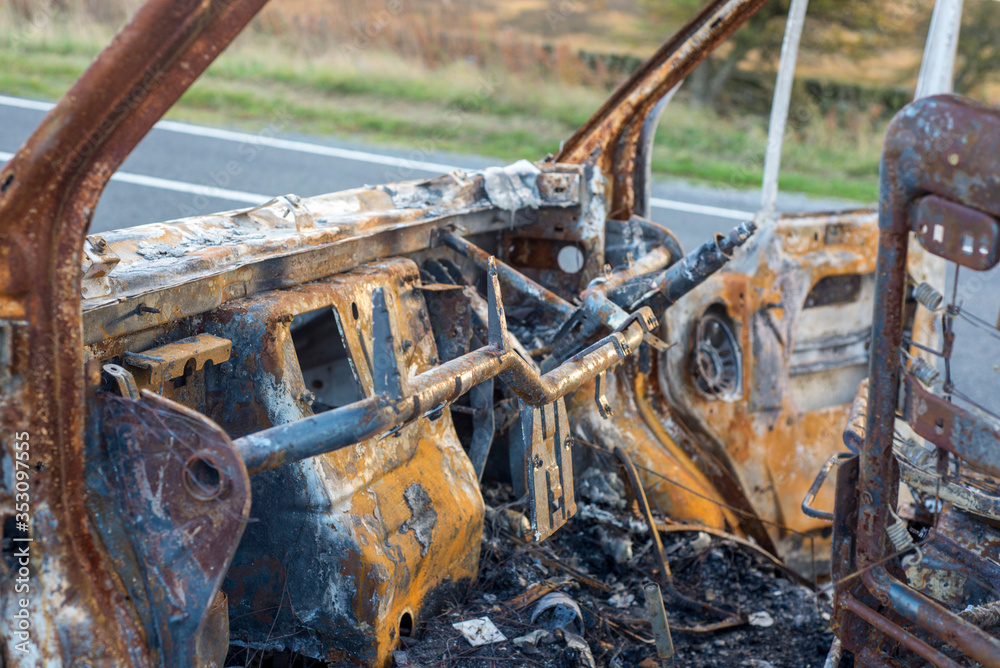 The burned out wreckage of an old van in a road layby 