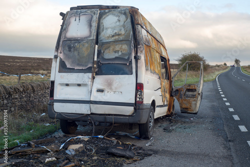 The burned out wreckage of an old van in a road layby 