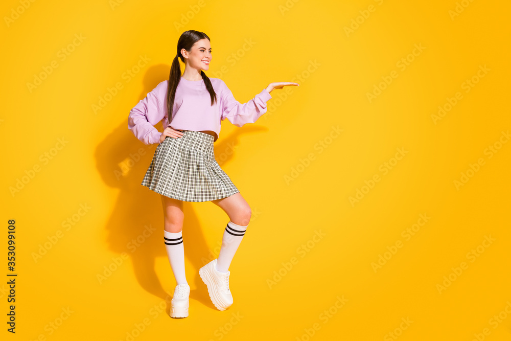 Full size photo of positive cheerful girl hold hand present ads promo recommend select suggest wear stylish style trendy checkered pullover isolated over bright shine color background Full size photo of positive cheerful girl hold hand present ads promo recommend select suggest wear stylish style trendy checkered pullover isolated over bright shine color background