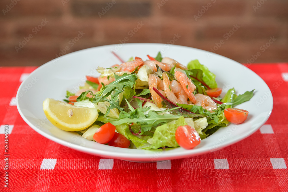Vegetable salad with shrimp on white plate on red-white tablecloth Vegetable salad with shrimp on white plate on red-white tablecloth