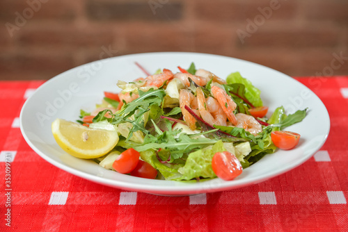 Vegetable salad with shrimp on white plate on red-white tablecloth