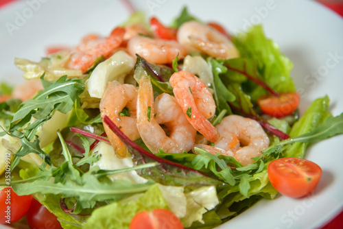 Vegetable salad with shrimp on white plate on red-white tablecloth